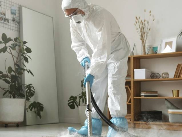 A person in protective suit cleans a carpet.